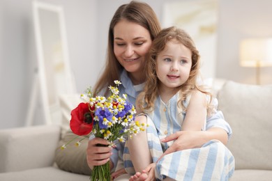 Photo of Mother and her little daughter with bouquet of beautiful flowers on sofa indoors