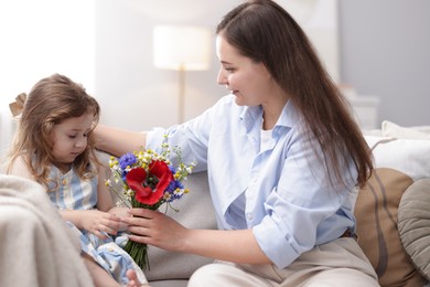 Photo of Mother and her little daughter with bouquet of beautiful flowers on sofa indoors