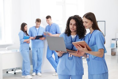 Photo of Medical students in uniforms with tablet and laptop indoors, selective focus