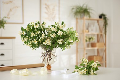 Photo of Bouquet of beautiful jasmine flowers in vase on white table indoors