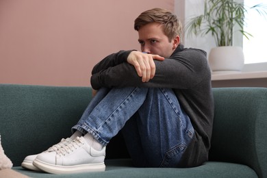 Photo of Man suffering from paranoia on sofa at home