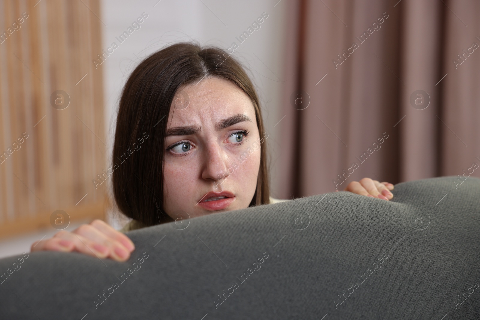 Paranoia. Worried woman hiding behind sofa indoors Photo of Paranoia. Worried woman hiding behind sofa indoors