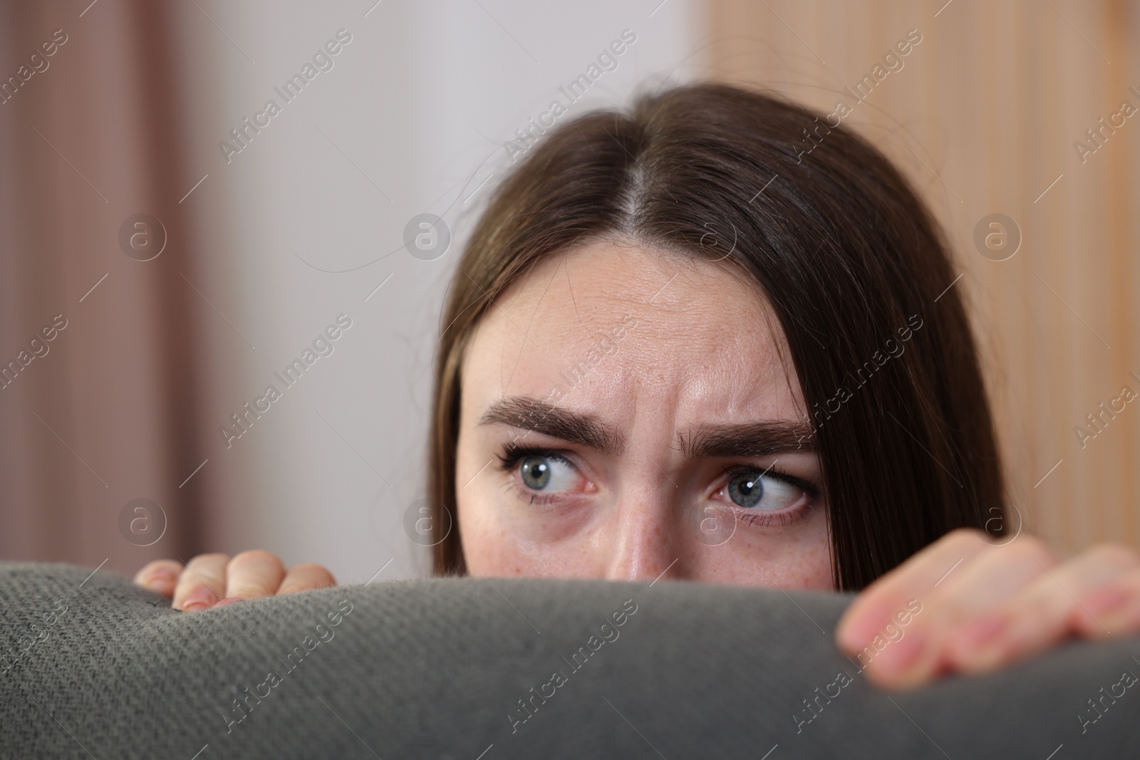 Paranoia. Worried woman hiding behind sofa indoors, closeup Photo of Paranoia. Worried woman hiding behind sofa indoors, closeup