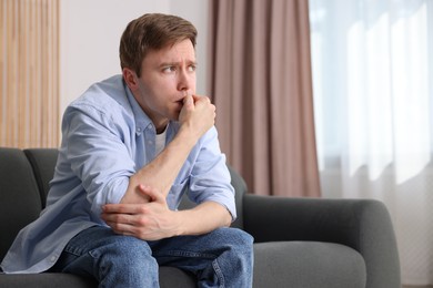 Photo of Man suffering from paranoia on sofa at home, space for text