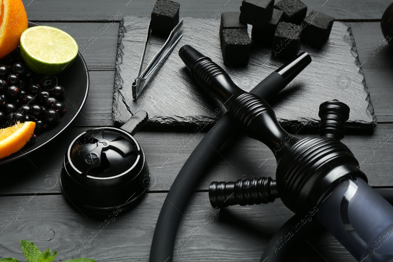 Photo of Hookah, coal and fresh fruits on black wooden table, closeup