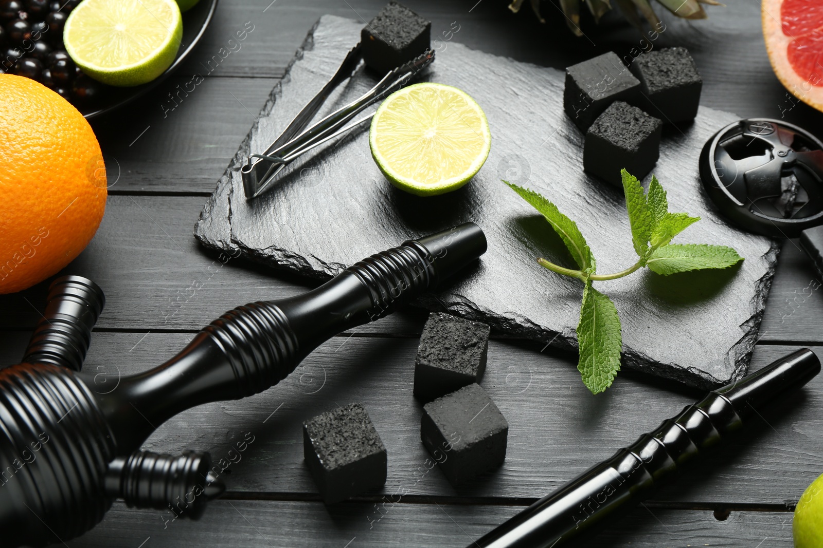 Photo of Hookah, coal and fresh fruits on black wooden table, closeup