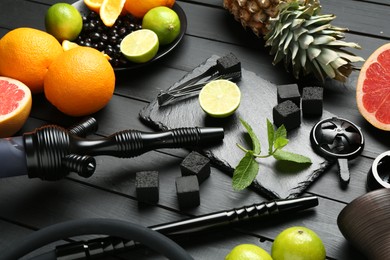 Photo of Hookah, coal and fresh fruits on black wooden table, closeup
