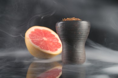 Photo of Hookah bowl with smoke and grapefruit on black table, closeup