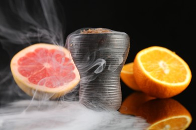 Photo of Hookah bowl with smoke and fruits on black table, closeup