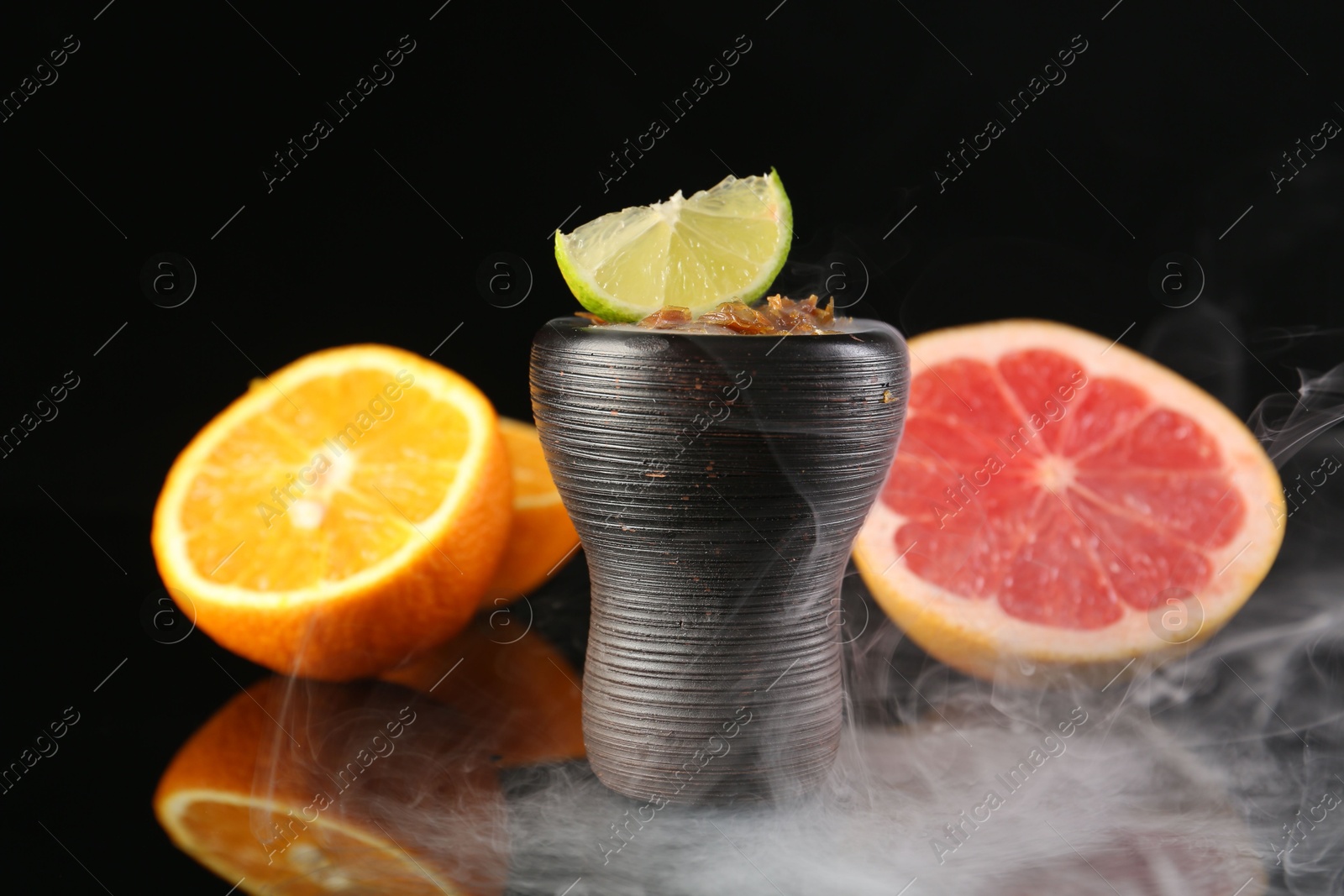 Photo of Hookah bowl with smoke and fruits on black table, closeup