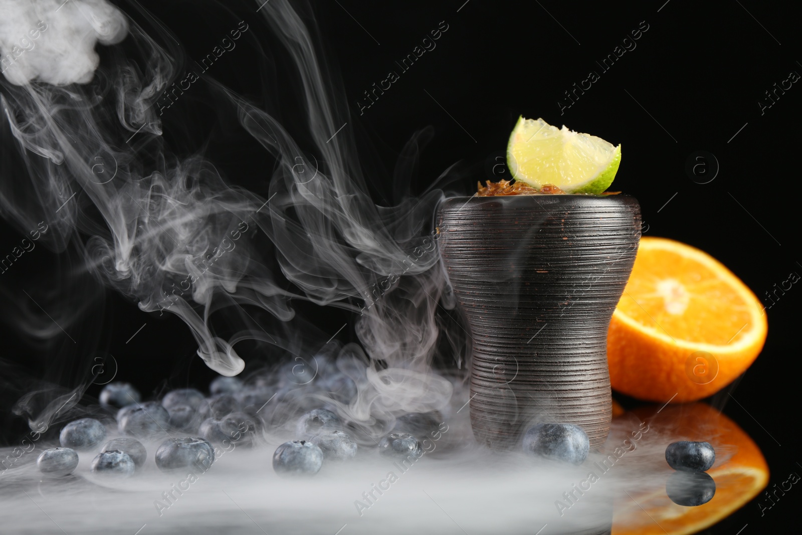 Photo of Hookah bowl with smoke and fruits on black table, closeup