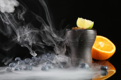 Photo of Hookah bowl with smoke and fruits on black table, closeup