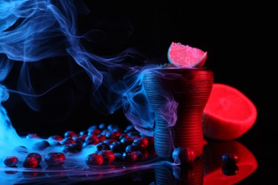 Photo of Hookah bowl with smoke and fruits on black table in neon lights, closeup