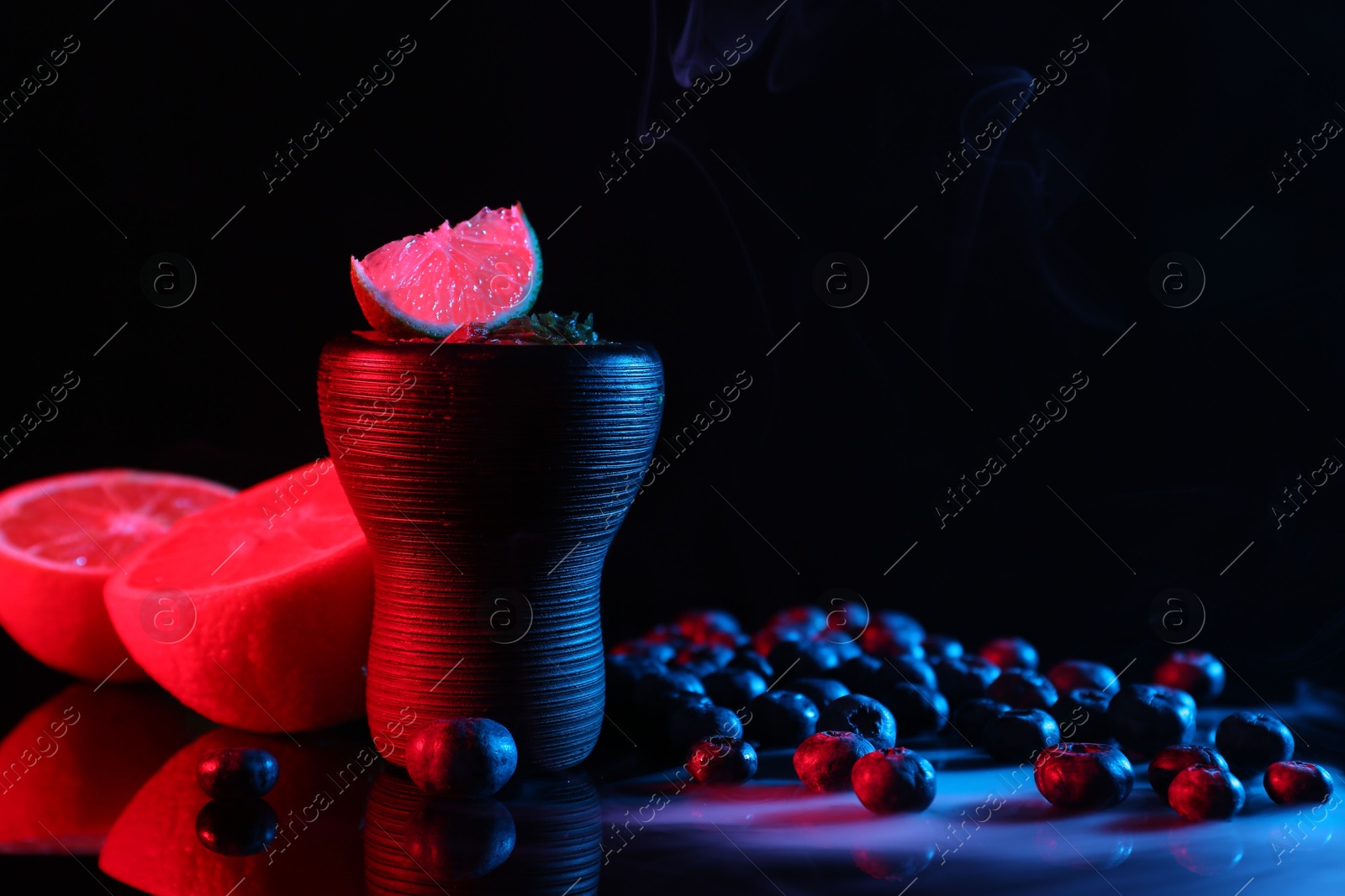 Photo of Hookah bowl with smoke and fruits on black table in neon lights, closeup. Space for text