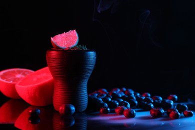 Photo of Hookah bowl with smoke and fruits on black table in neon lights, closeup. Space for text