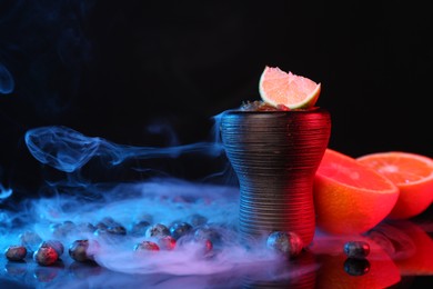 Photo of Hookah bowl with smoke and fruits on black table in neon lights, closeup