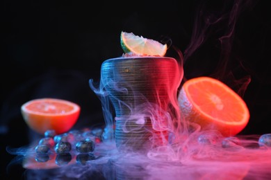 Photo of Hookah bowl with smoke and fruits on black table in neon lights, closeup