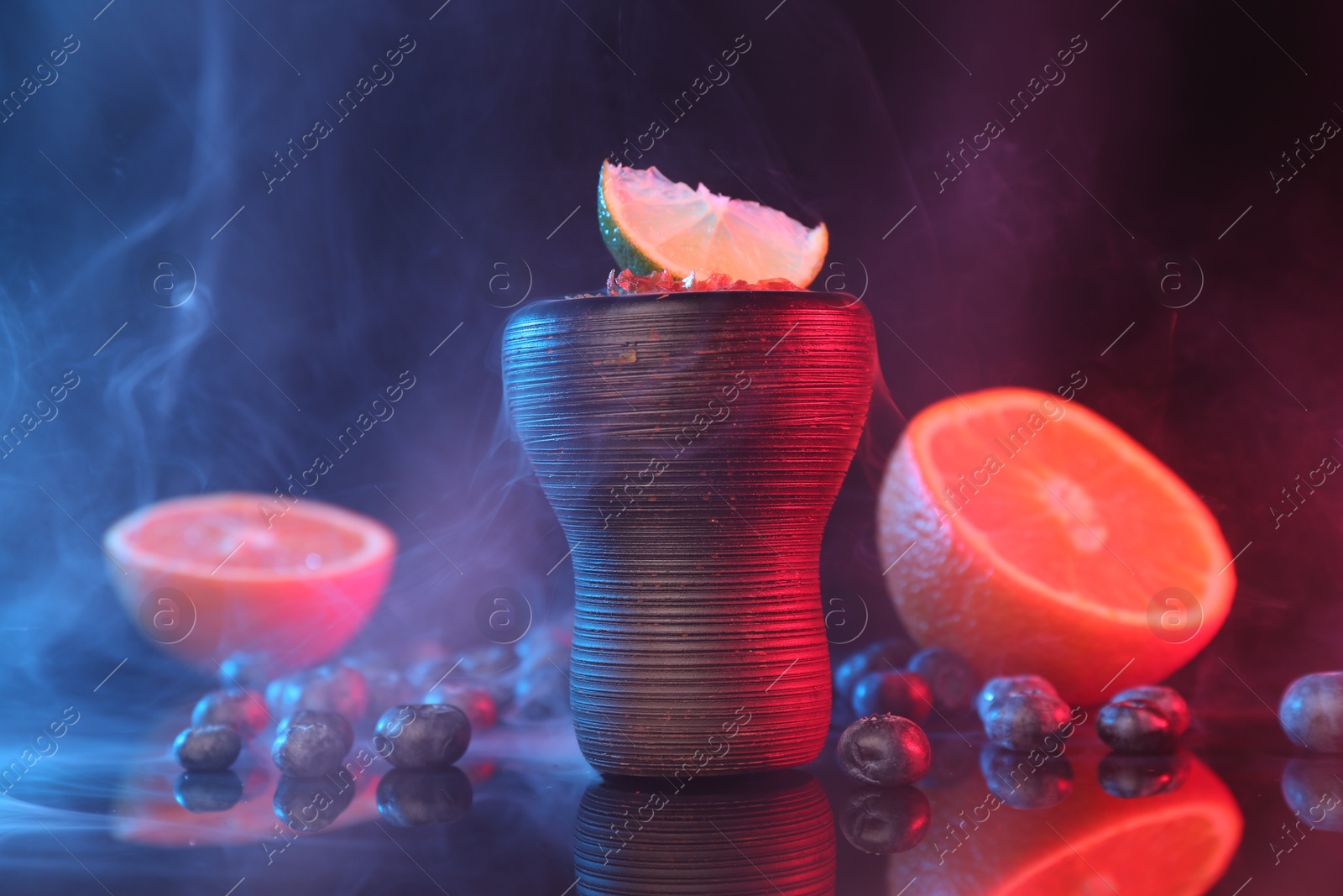 Photo of Hookah bowl with smoke and fruits on black table in neon lights, closeup