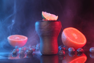 Photo of Hookah bowl with smoke and fruits on black table in neon lights, closeup