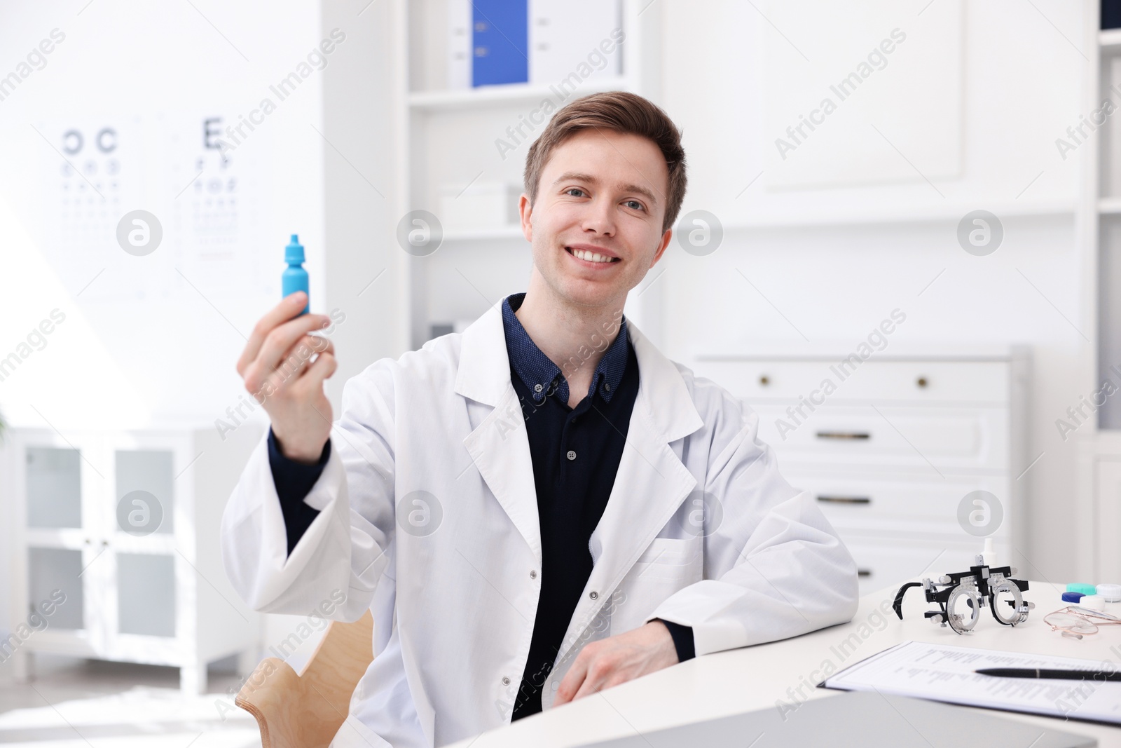 Portrait of professional ophthalmologist with eye drops at white table in clinic Photo of Portrait of professional ophthalmologist with eye drops at white table in clinic
