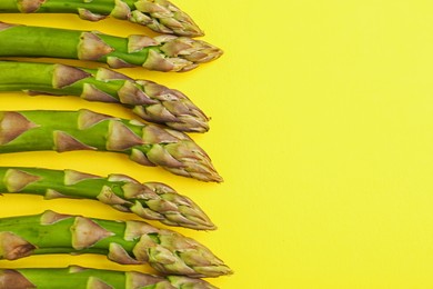Photo of Fresh ripe raw asparagus on yellow background, flat lay. Space for text