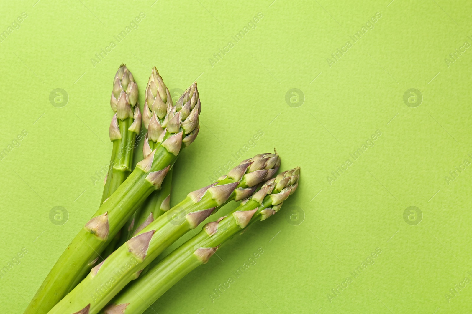 Fresh ripe raw asparagus on green background, top view. Space for text Photo of Fresh ripe raw asparagus on green background, top view. Space for text