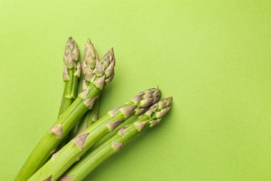Photo of Fresh ripe raw asparagus on green background, top view. Space for text