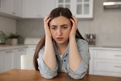 Photo of Woman suffering from paranoia at table in kitchen