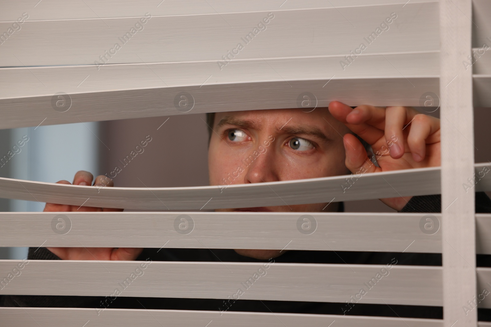 Paranoia. Worried man looking through window blinds indoors, closeup Photo of Paranoia. Worried man looking through window blinds indoors, closeup