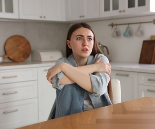Photo of Worried woman suffering from paranoia at table in kitchen