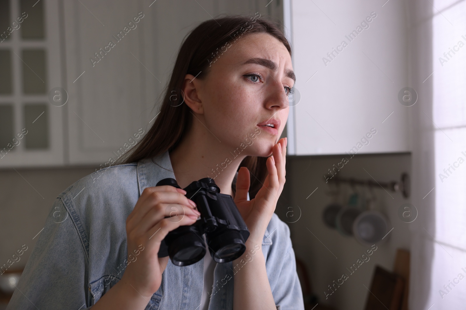 Paranoia. Worried woman with binoculars in kitchen Photo of Paranoia. Worried woman with binoculars in kitchen