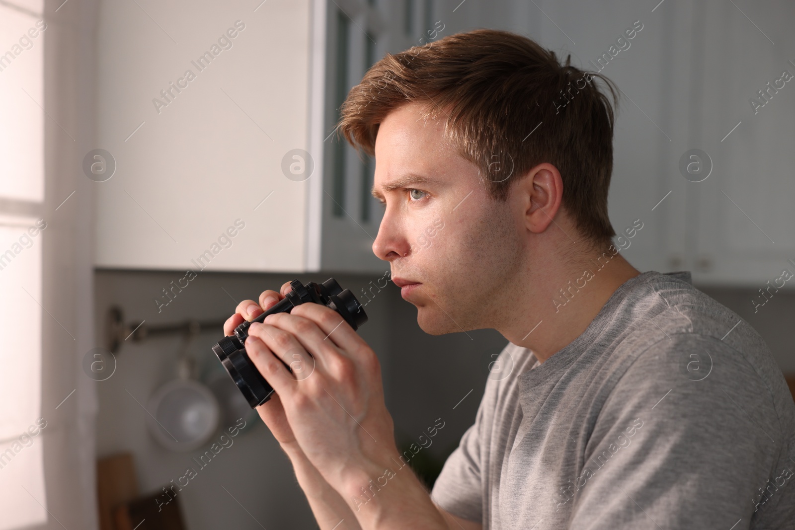 Paranoia. Worried man with binoculars in kitchen Photo of Paranoia. Worried man with binoculars in kitchen