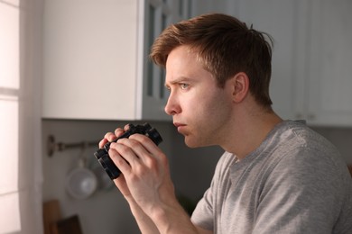 Photo of Paranoia. Worried man with binoculars in kitchen