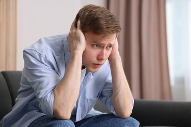 Photo of Man suffering from paranoia on sofa at home, space for text