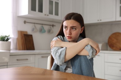 Photo of Worried woman suffering from paranoia at table in kitchen