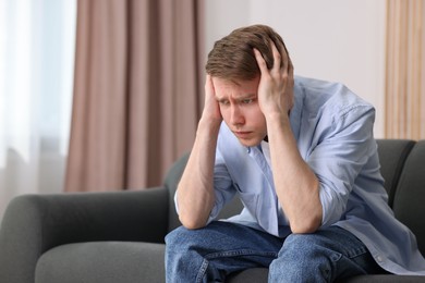 Photo of Man suffering from paranoia on sofa at home, space for text