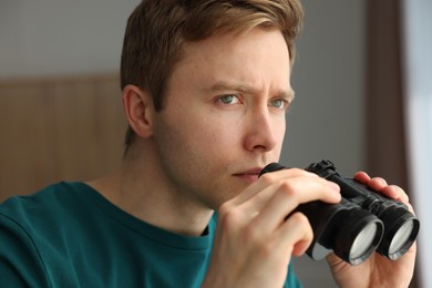 Photo of Paranoia. Worried man with binoculars at home