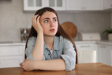 Photo of Scared woman suffering from paranoia at table in kitchen