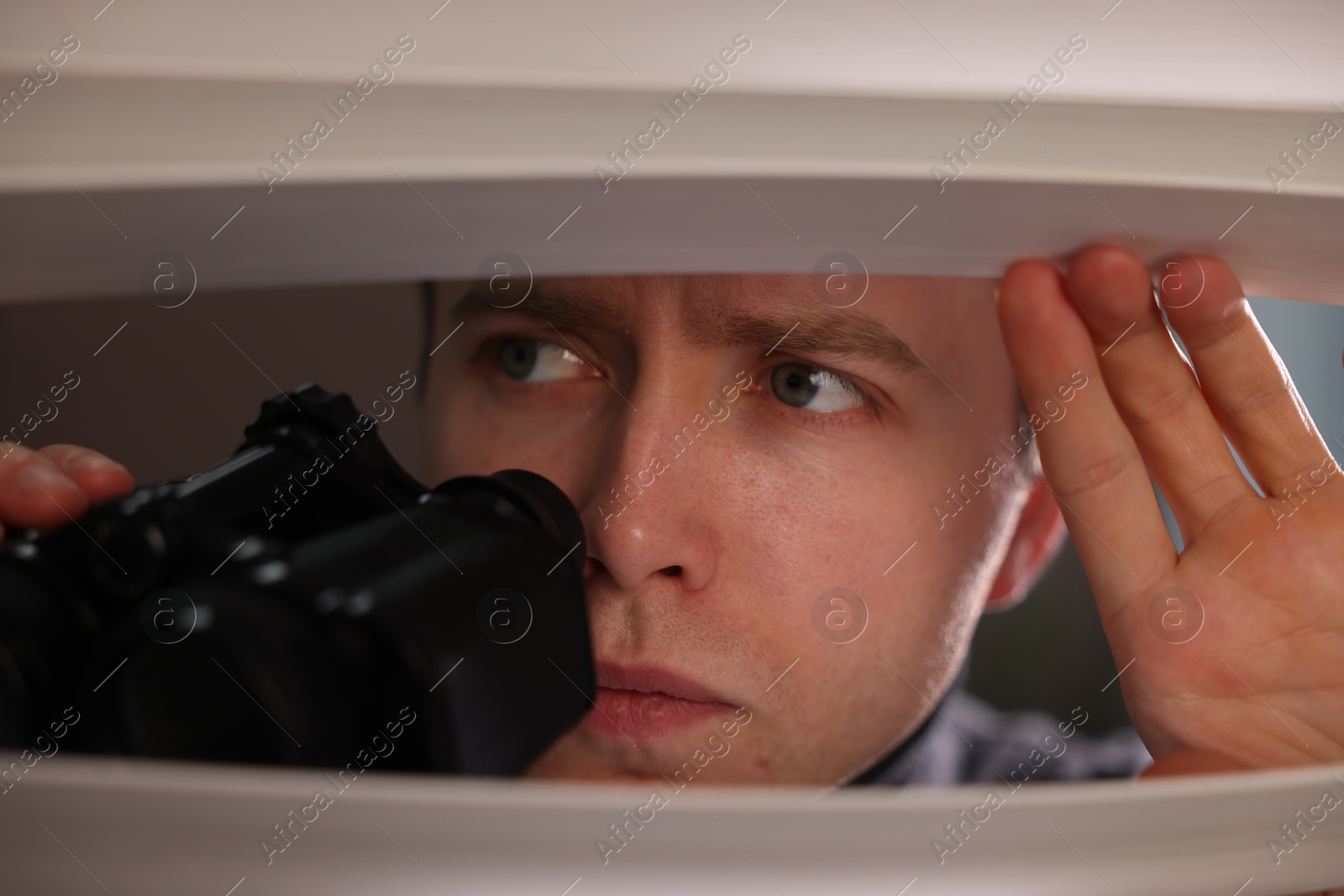 Paranoia. Worried man with binoculars looking through window blinds indoors Photo of Paranoia. Worried man with binoculars looking through window blinds indoors
