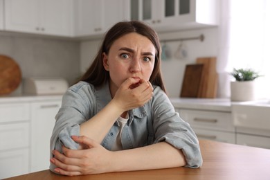 Photo of Scared woman suffering from paranoia at table in kitchen
