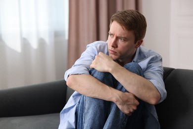 Photo of Man suffering from paranoia on sofa at home, space for text