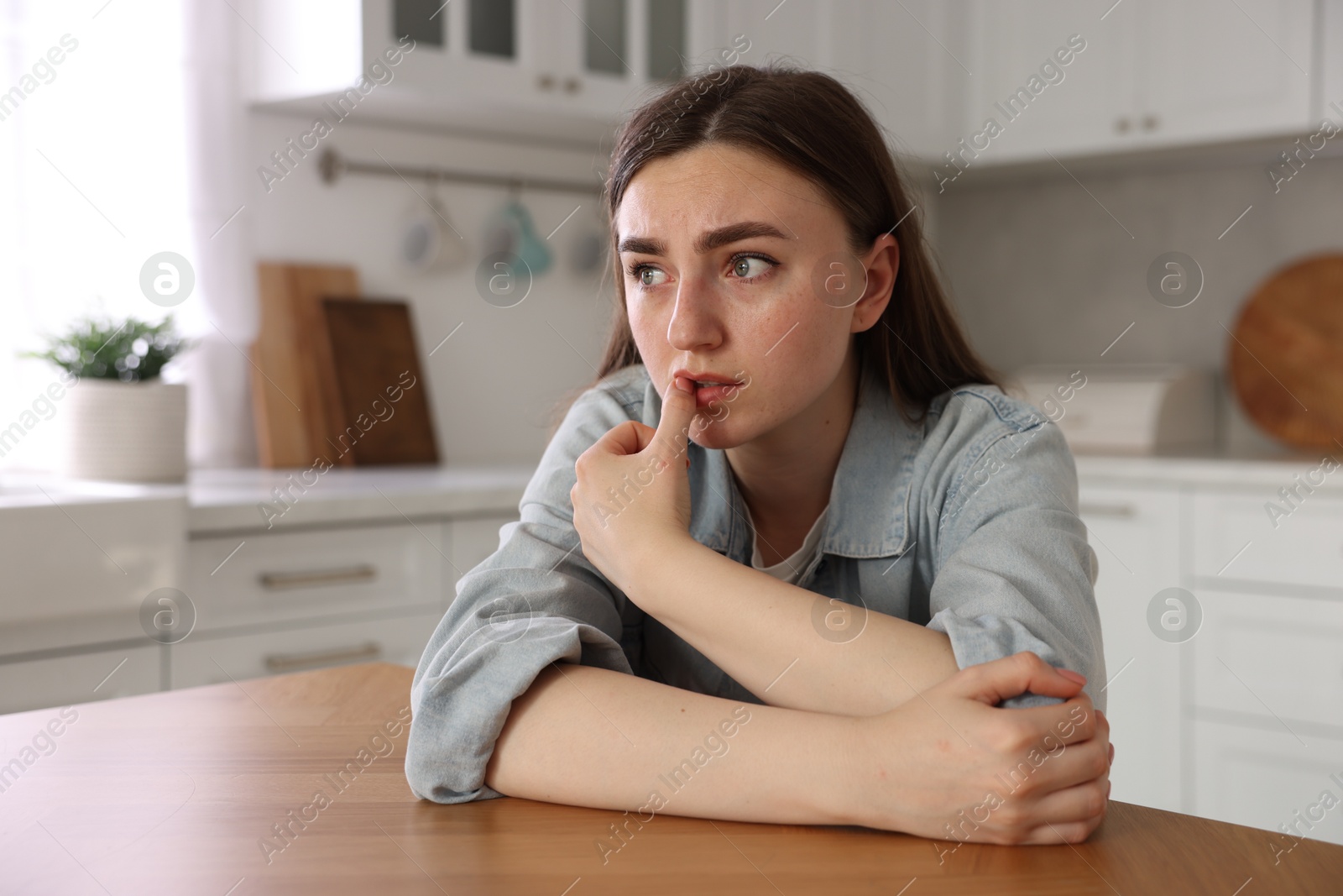 Scared woman suffering from paranoia at table in kitchen Photo of Scared woman suffering from paranoia at table in kitchen