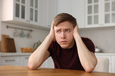 Photo of Man suffering from paranoia at table in kitchen