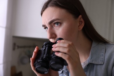 Photo of Paranoia. Worried woman with binoculars in kitchen