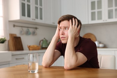 Photo of Scared man suffering from paranoia at wooden table in kitchen