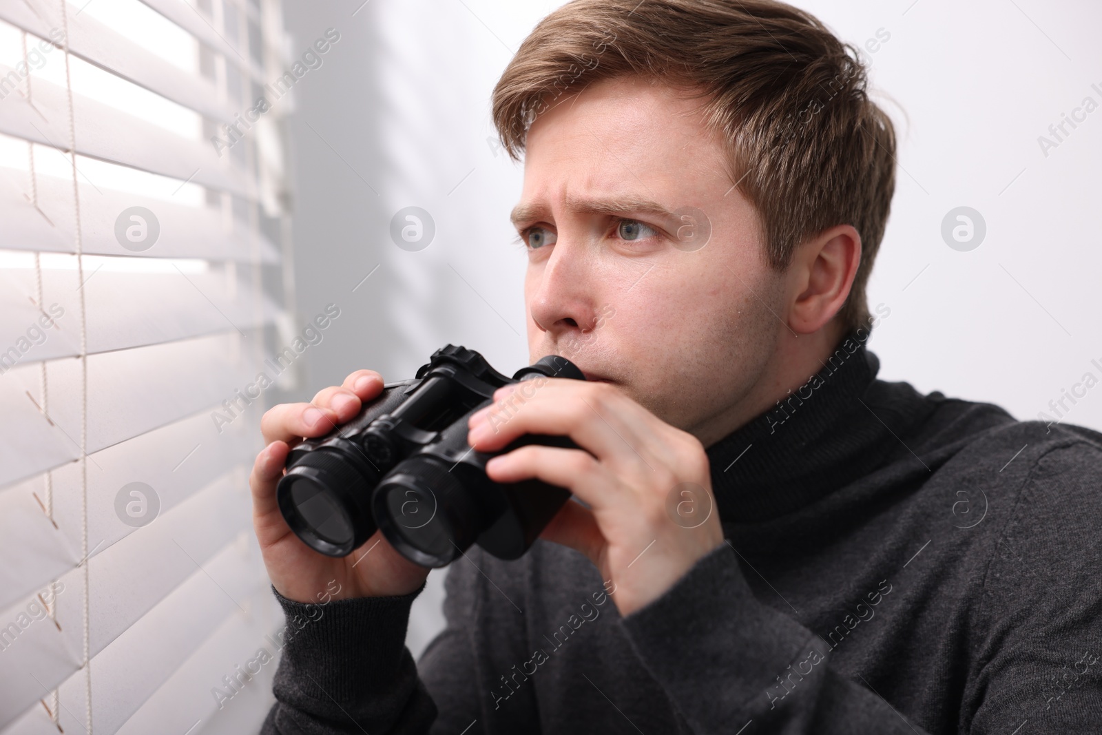 Paranoia. Worried man with binoculars near window indoors Photo of Paranoia. Worried man with binoculars near window indoors