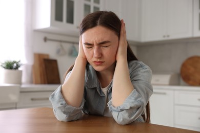 Photo of Scared woman suffering from paranoia at wooden table in kitchen