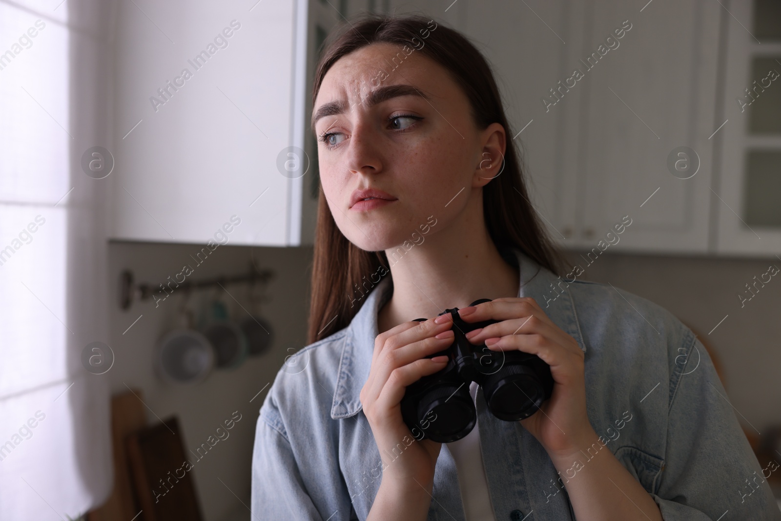 Paranoia. Worried woman with binoculars in kitchen, space for text Photo of Paranoia. Worried woman with binoculars in kitchen, space for text