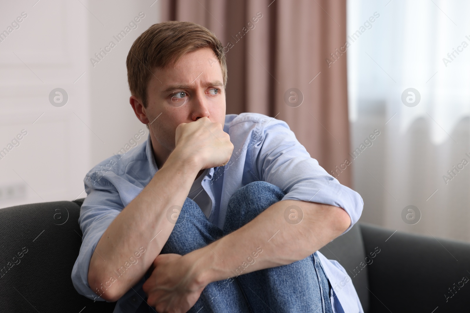 Scared man suffering from paranoia on sofa at home Photo of Scared man suffering from paranoia on sofa at home
