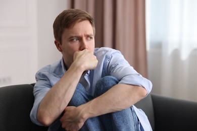 Photo of Scared man suffering from paranoia on sofa at home